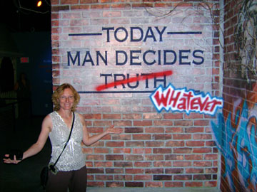 The author's wife poses before a display announcing "Today Man Decides Truth," with "Truth" replaced with "Whatever."