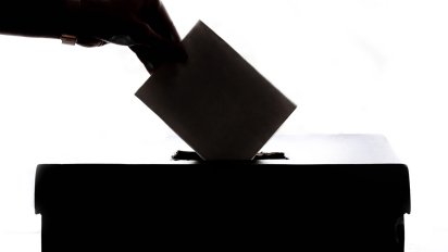 A hand putting a ballot into a box.