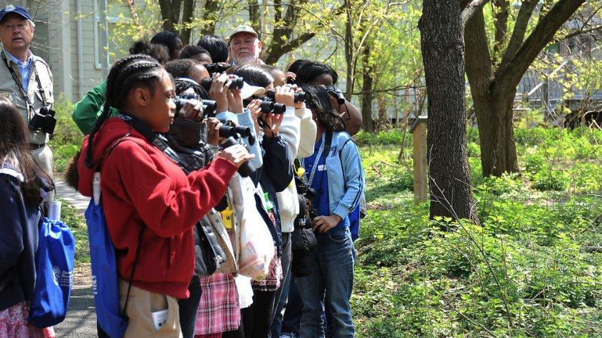 Young people using binoculars in a forest setting.